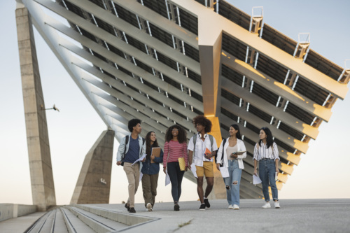 A group of students walk together underneath a large solar panel in a concreted area.