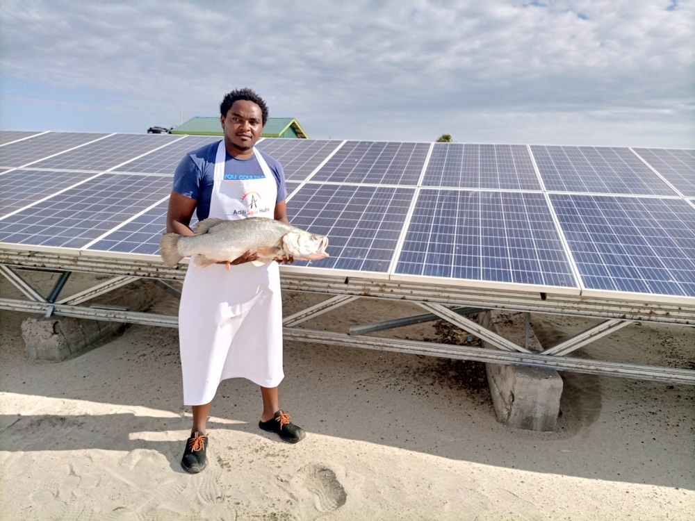 A man standing in front of a solar panel holding a fish