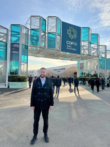 Jakub Vrba standing at the entrance to COP29 in Baku, Azerbaijan