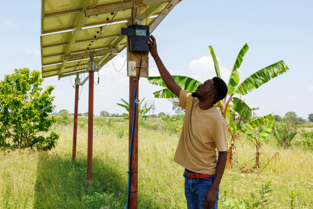 A Simusolar technician on a farm in Tanzania, reaching for the control panel of a solar panel
