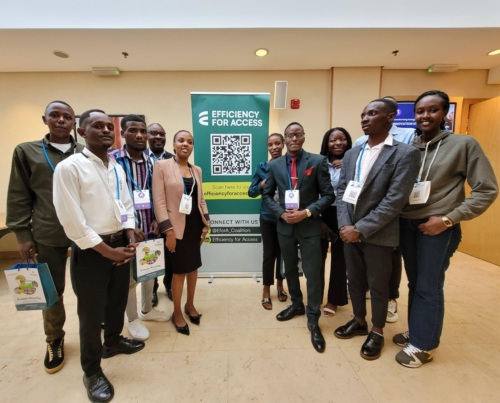 A group of students from the University of Rwanda, attending the TEA Forum, standing in front of an Efficiency for Access banner.